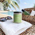 Handmade Cucumber Mint Spritz beeswax and tallow candle displayed poolside on a white towel beside sunglasses.