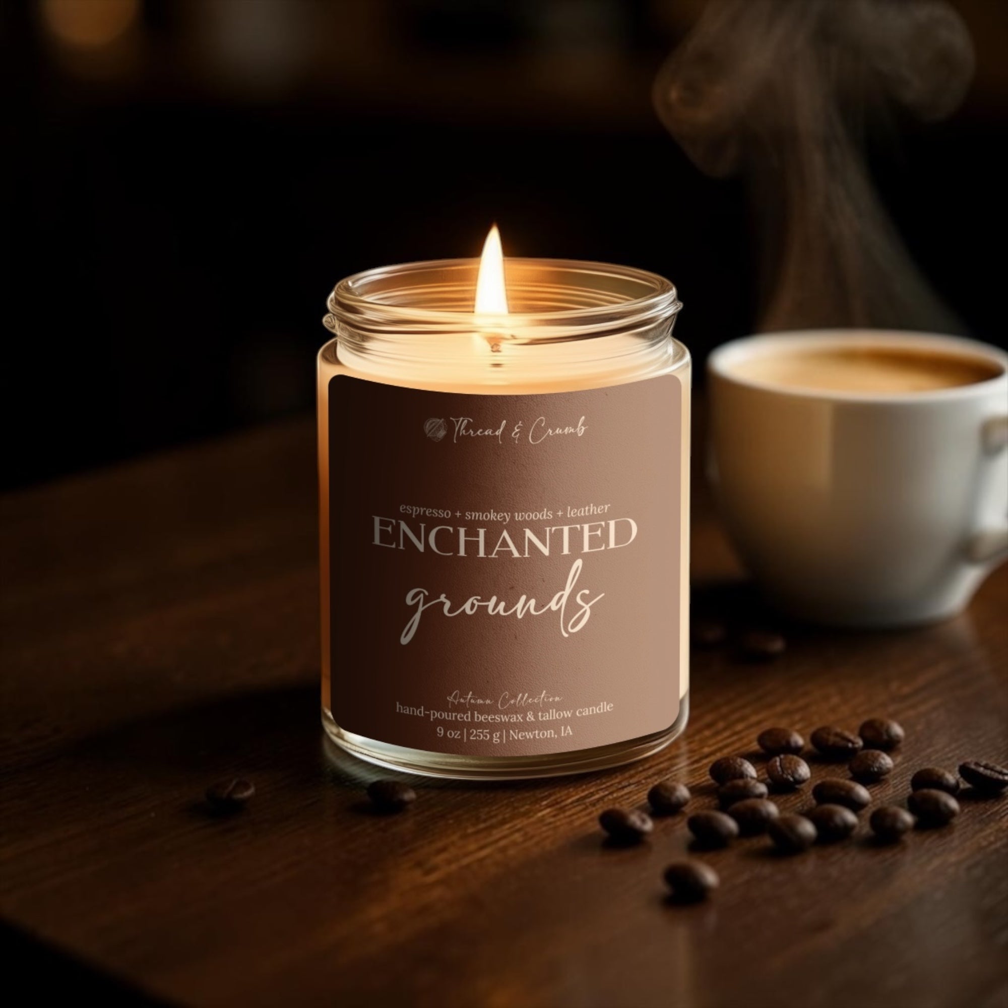 A lit jar candle labeled 'Enchanted Grounds' by Thread & Crumb sits on a dark wooden table with scattered coffee beans, with a cup of coffee blurred in the background.
