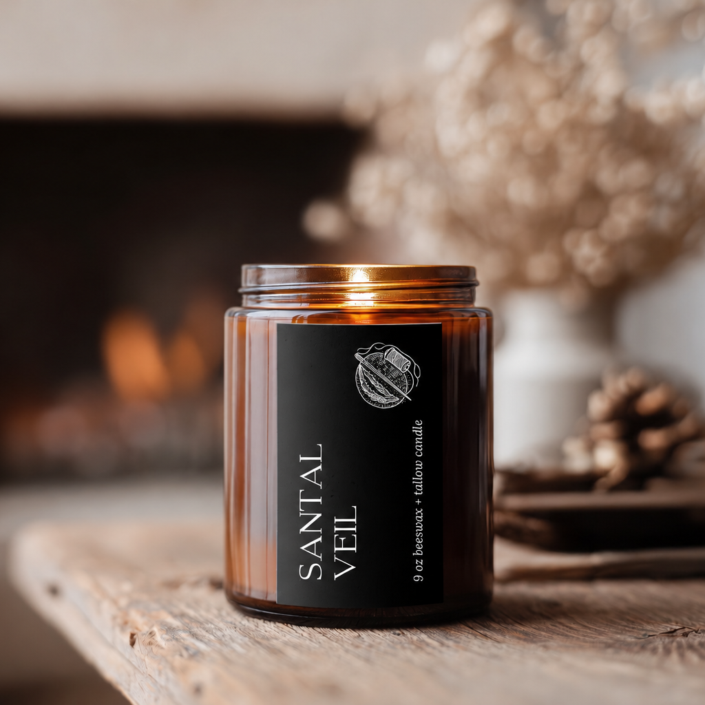 Santal Veil sandalwood candle in an amber glass jar on a rustic wooden table beside a softly glowing fireplace