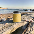 Handmade Sol Coast beeswax and tallow candle displayed on driftwood overlooking the beach.