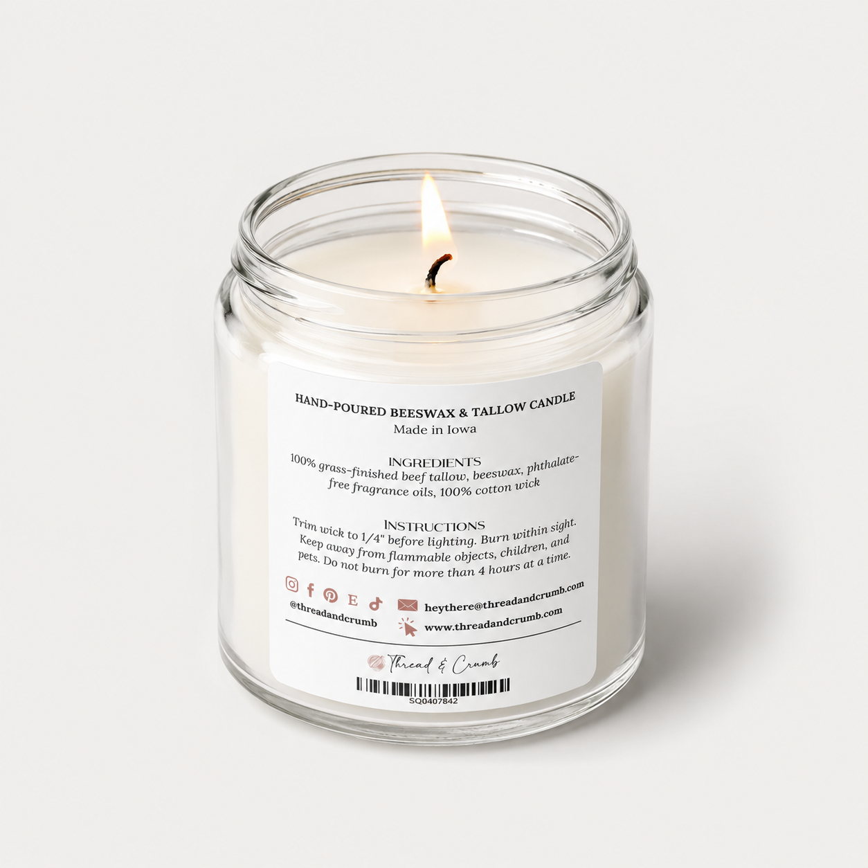 A lit hand-poured Thread & Crumb branded beeswax and tallow candle in a clear glass jar with a white label showing product details, set against a clean white background.